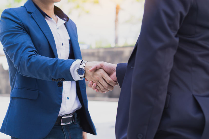 Two business man making handshake in the city. Business etiquett Two people in suits are shaking hands outdoors, with one wearing a blue suit and the other a dark suit.